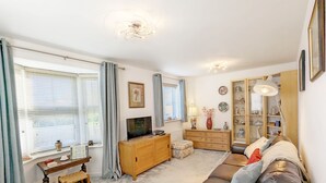 A living room with a brown leather sofa, a wooden cabinet, a television, and a window with blinds.