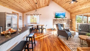 A spacious kitchen with a wooden ceiling, a dining area with a large TV, and a cozy living room with seating. - STUNNING SMOKY MOUNTAIN VIEWS! Hot Tub! Games! Close to Dollywood and Parkway! (Sevierville)