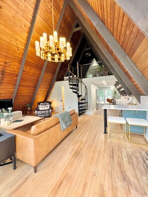 Un espace de vie de style loft avec un plafond en bois, un canapé, une table à manger et un escalier menant à un niveau supérieur.