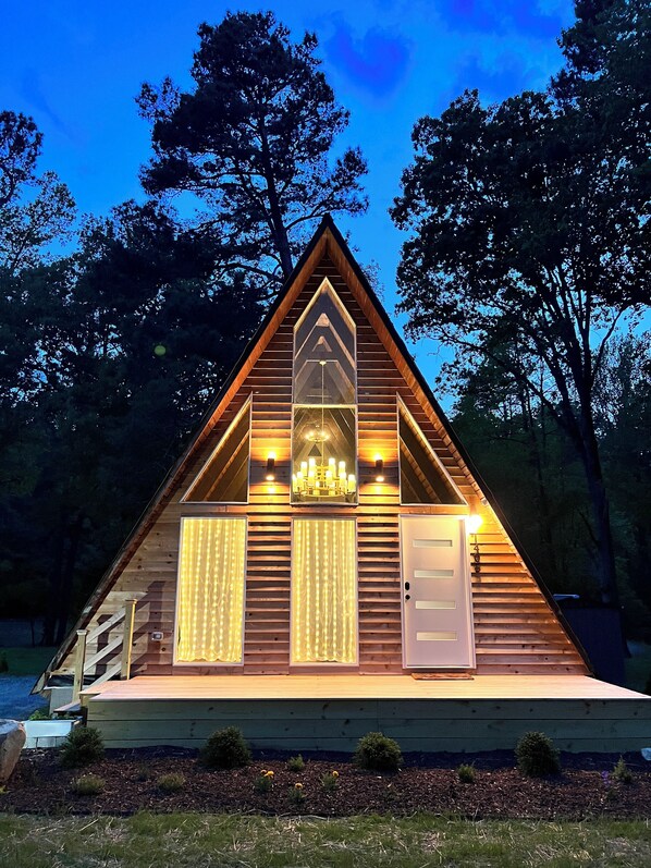 A triangular wooden cabin with a central skylight, a chandelier, and a door.