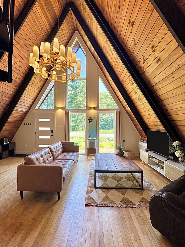 Ein geräumiges Dachzimmer mit geneigter Decke, einem Ledersofa, einem Couchtisch und einem Fernseher auf einem Holzboden.