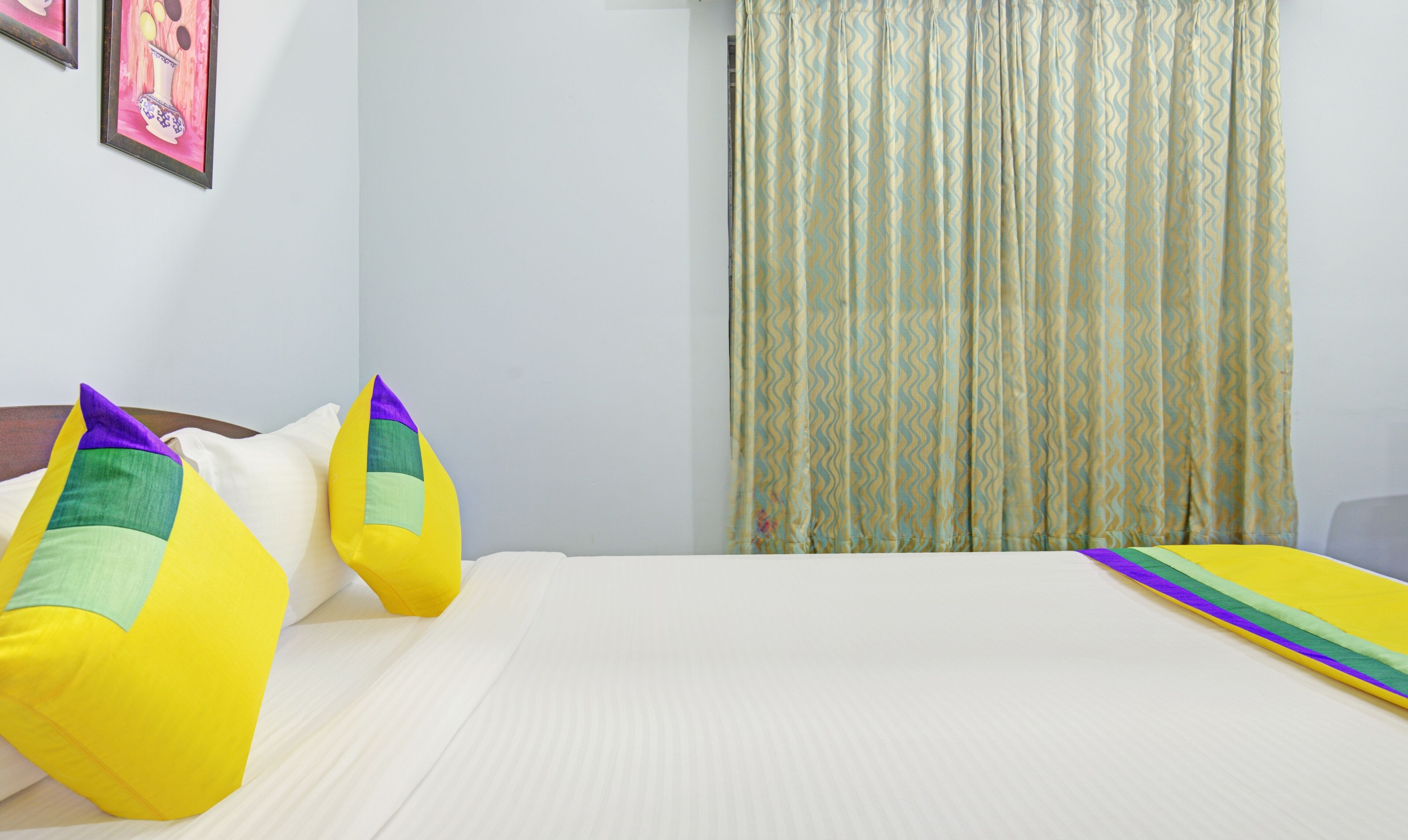 Une chambre d’hôtel avec un lit, des oreillers, un rideau et un mur orné d’un tableau.