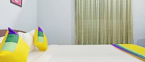 Una habitación de hotel con una cama, almohadas, una cortina y una pared con un cuadro.