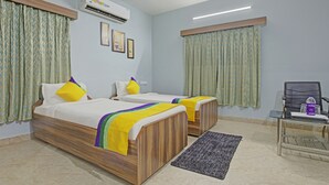A hotel room with two wooden beds, a small table with a chair, an air conditioner, and a window with curtains. - Itsy Hotels Sidhartha Residency (Bhubaneshwar)