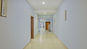 A hallway with light blue walls, a tiled floor, and framed pictures on the walls. - Itsy Hotels Sidhartha Residency (Bhubaneshwar)