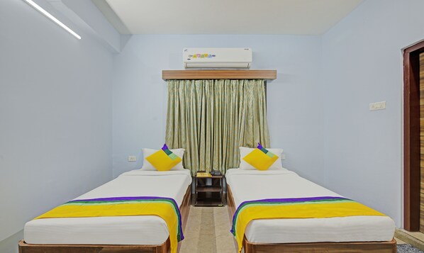 A room with two single beds, a small table, an air conditioning unit, and a curtain.