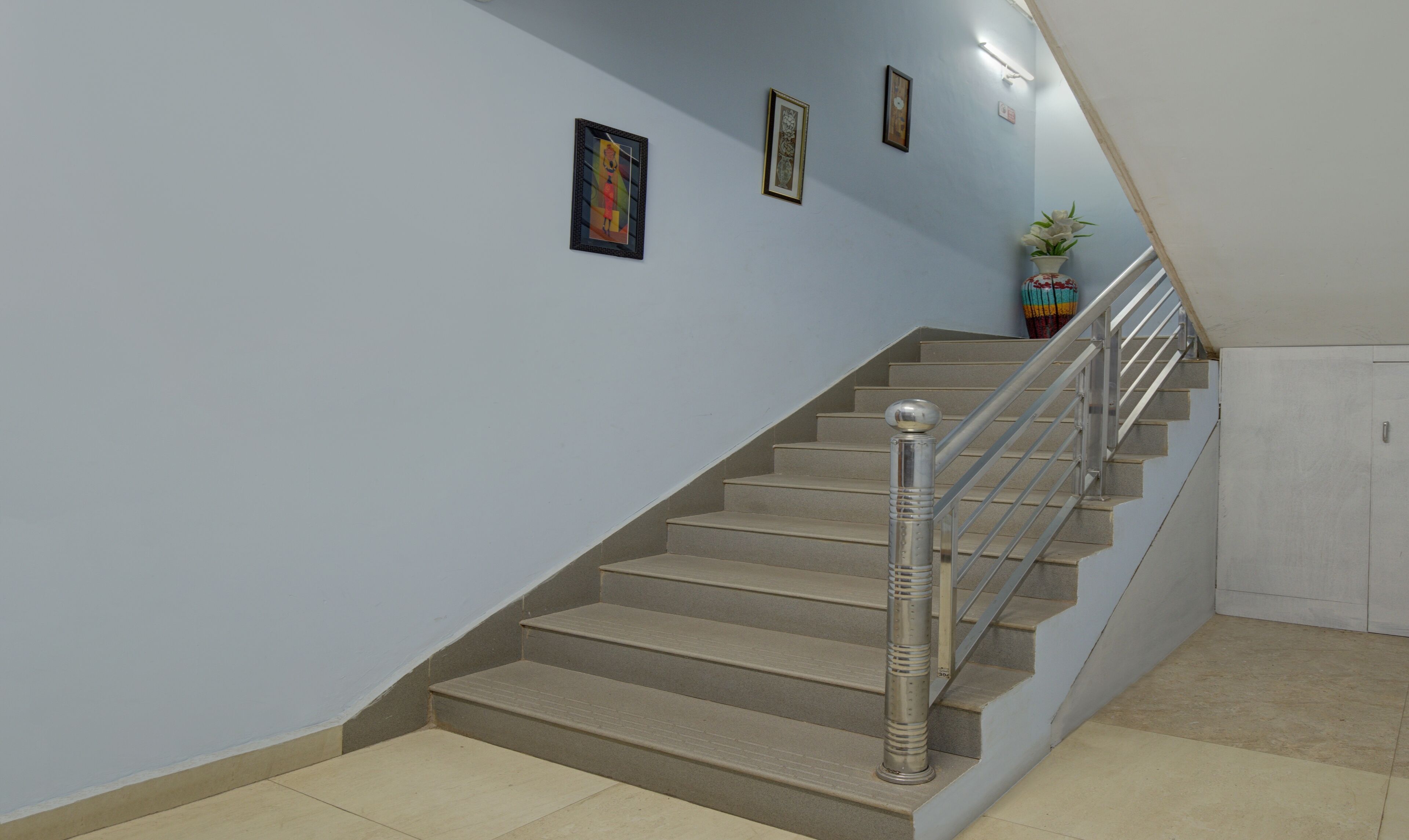 Una escalera con barandilla de metal, escalones color beige y pared azul claro.