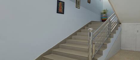 Una escalera con barandilla de metal, escalones color beige y pared azul claro.