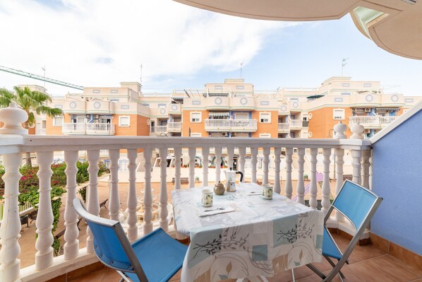 A balcony with a table set for two, chairs, and a view of apartment buildings.