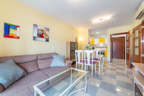 A living room with a sofa, a glass coffee table, and a dining area with chairs and a table.