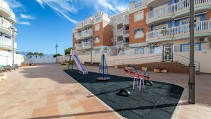 Un terrain de jeux avec un toboggan et des balançoires, entouré d’immeubles à plusieurs étages dotés de balcons.