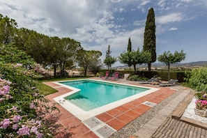 A rectangular swimming pool with a tiled deck, surrounded by trees and a grassy area.