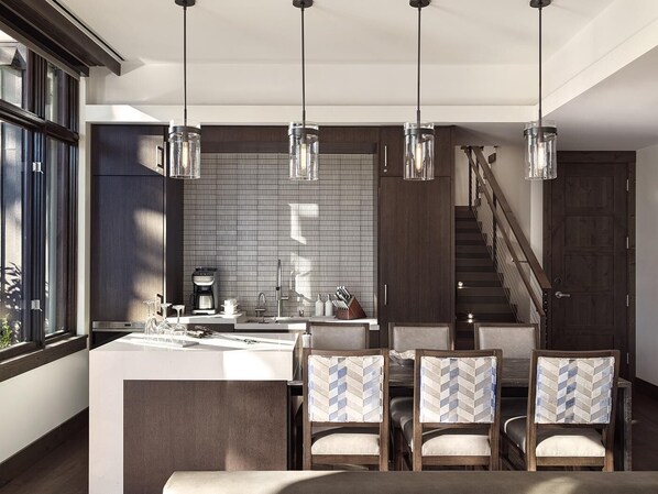 A modern kitchen with a central island, pendant lights, and a staircase leading to an upper level.