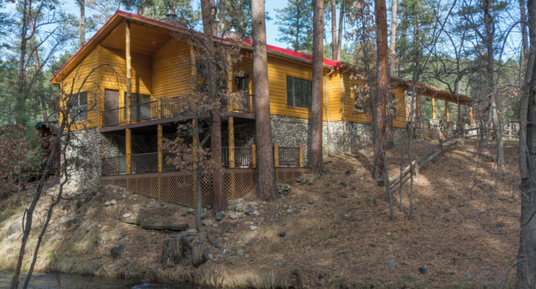 A log cabin with a balcony, surrounded by trees and a rocky landscape.