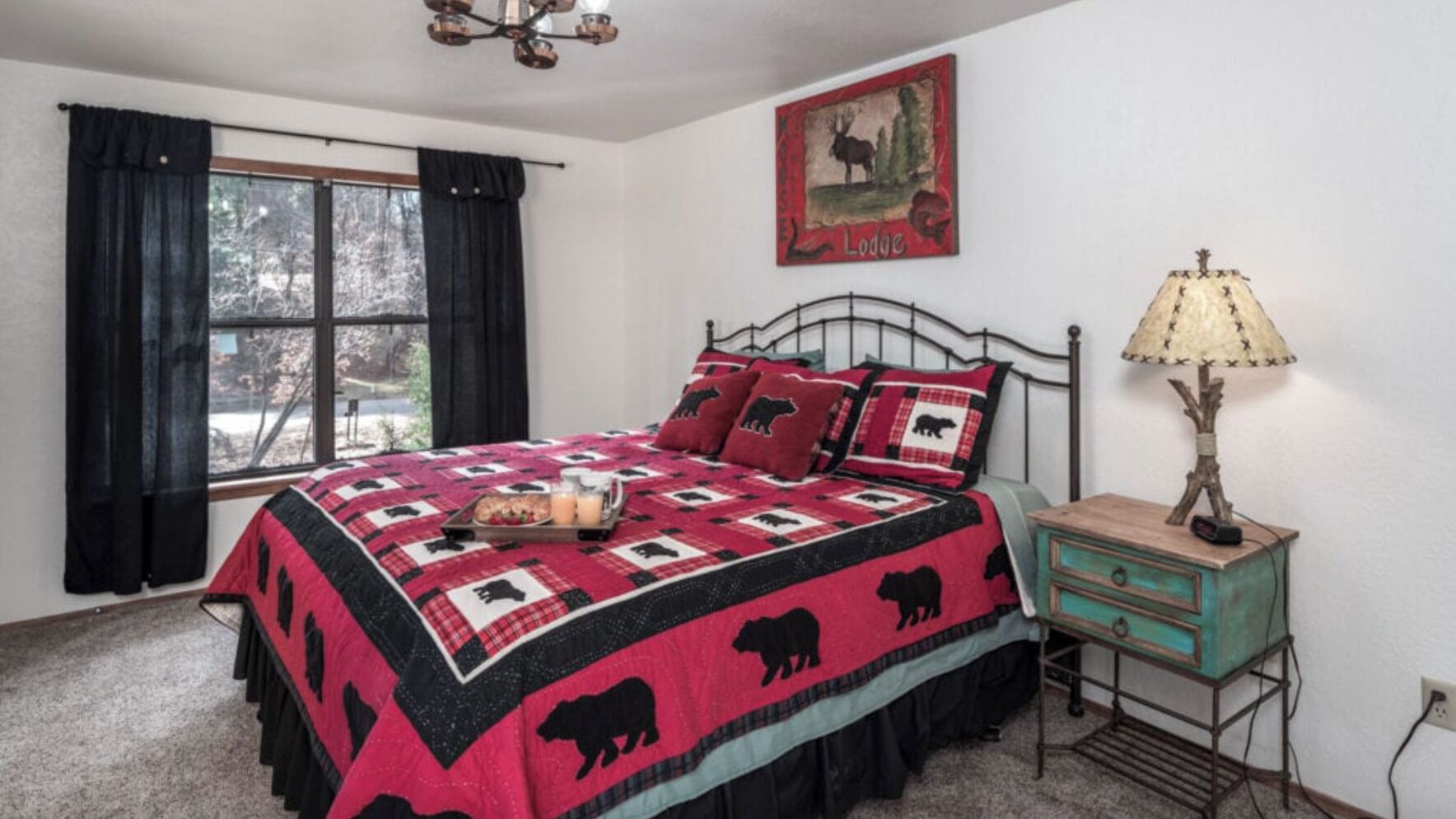 A bedroom with a bed, a nightstand, a lamp, a window with curtains, and a wall decoration.