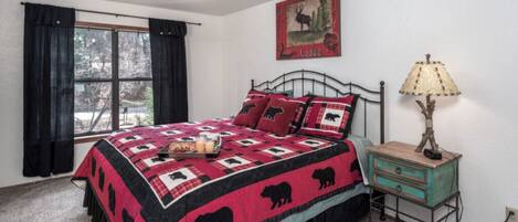 A bedroom with a bed, a nightstand, a lamp, a window with curtains, and a wall decoration.