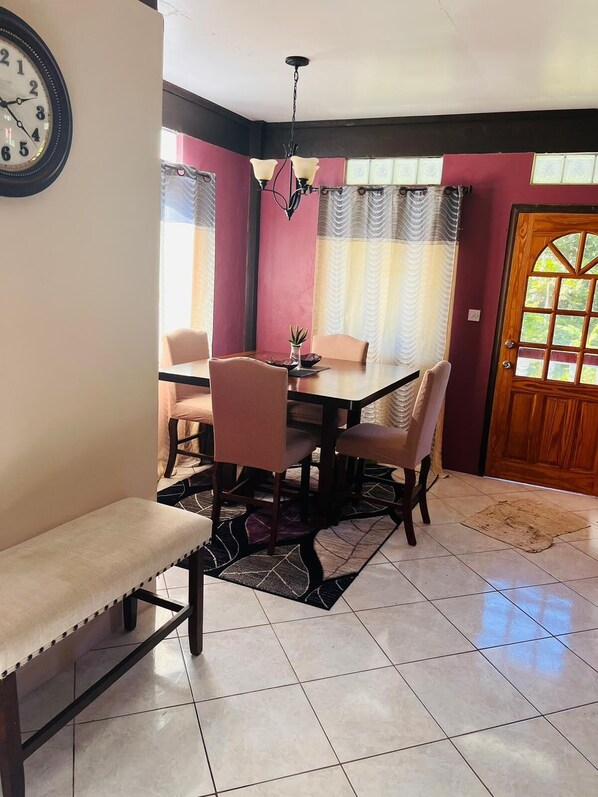 Un comedor con una mesa de madera, cuatro sillas, un banco, un reloj y una lámpara de araña.