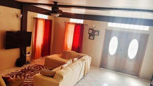 A living room with a sofa, a television, a ceiling fan, and a door with glass panels. - Nature's Luxurious Living (Roseau)