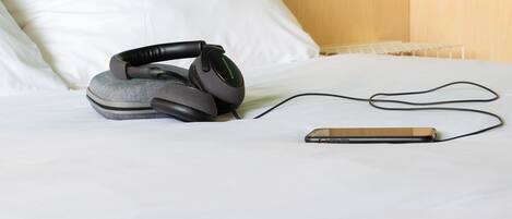 A bed with white sheets, a smartphone, and a pair of headphones on it.