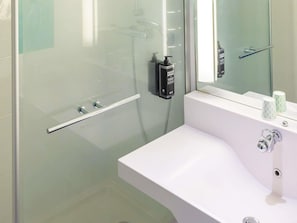 Ein modernes Badezimmer mit einer Duschkabine aus Glas, einem weißen Waschbecken und einem Spiegel.