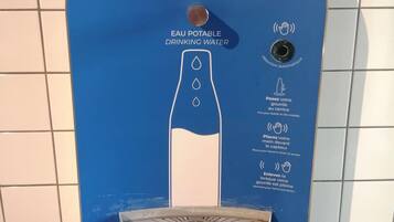 Dispensador de agua azul con instrucciones de uso, un sensor de movimiento y un grifo dosificador.