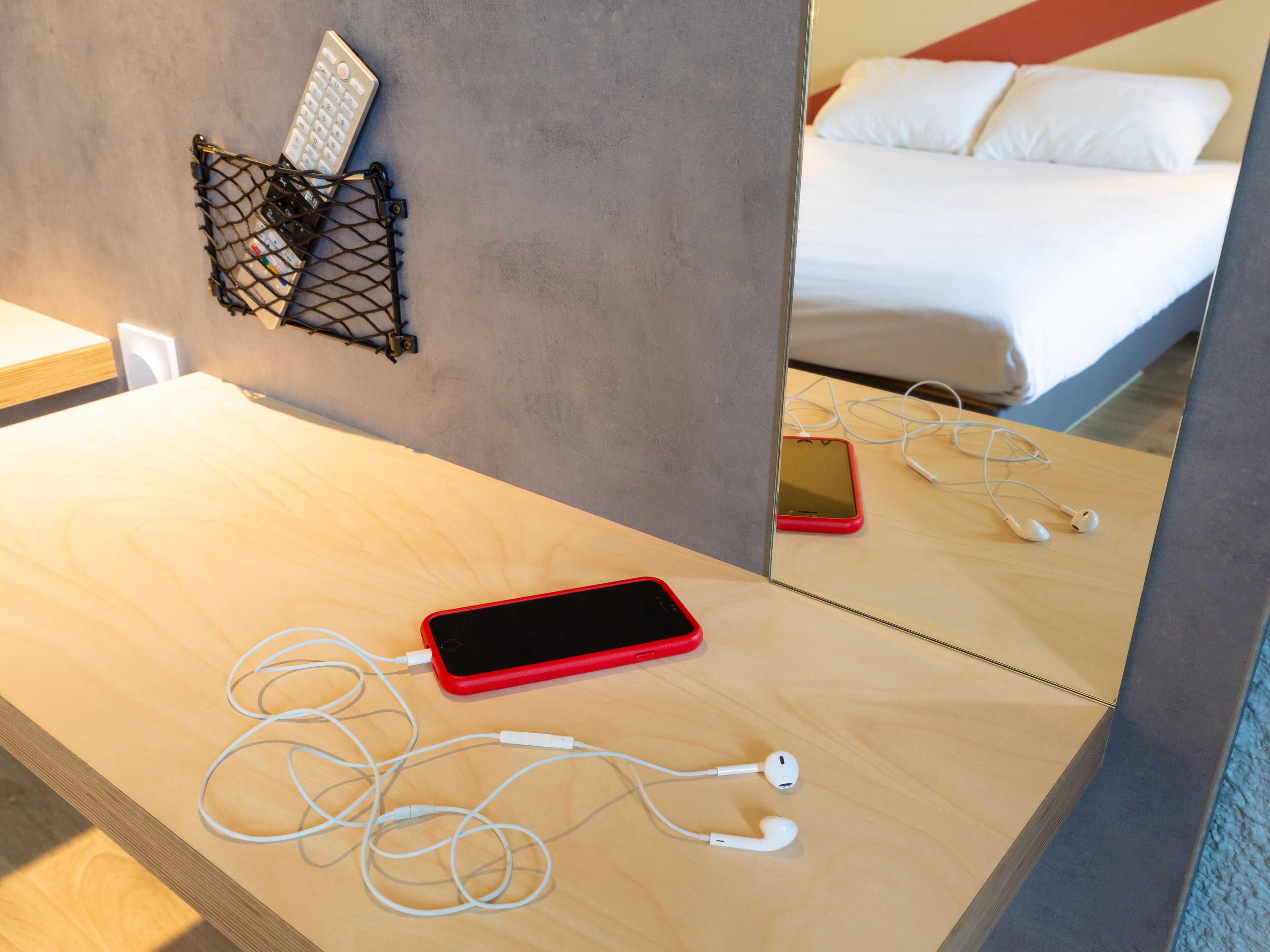 Habitación de hotel con un escritorio de madera, un teléfono inteligente rojo, auriculares blancos y un cable de carga negro.