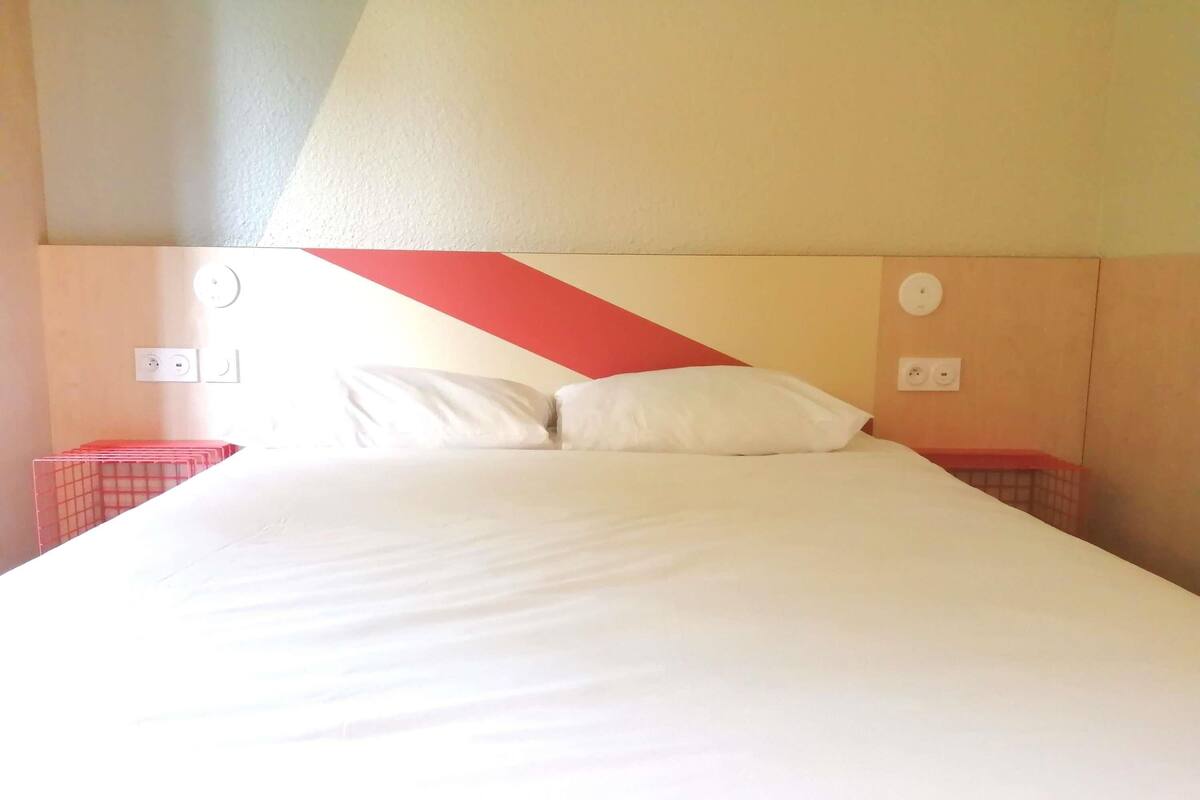 Ein Bett mit weißer Bettwäsche, zwei Nachttische und eine Wand mit geometrischem Muster.