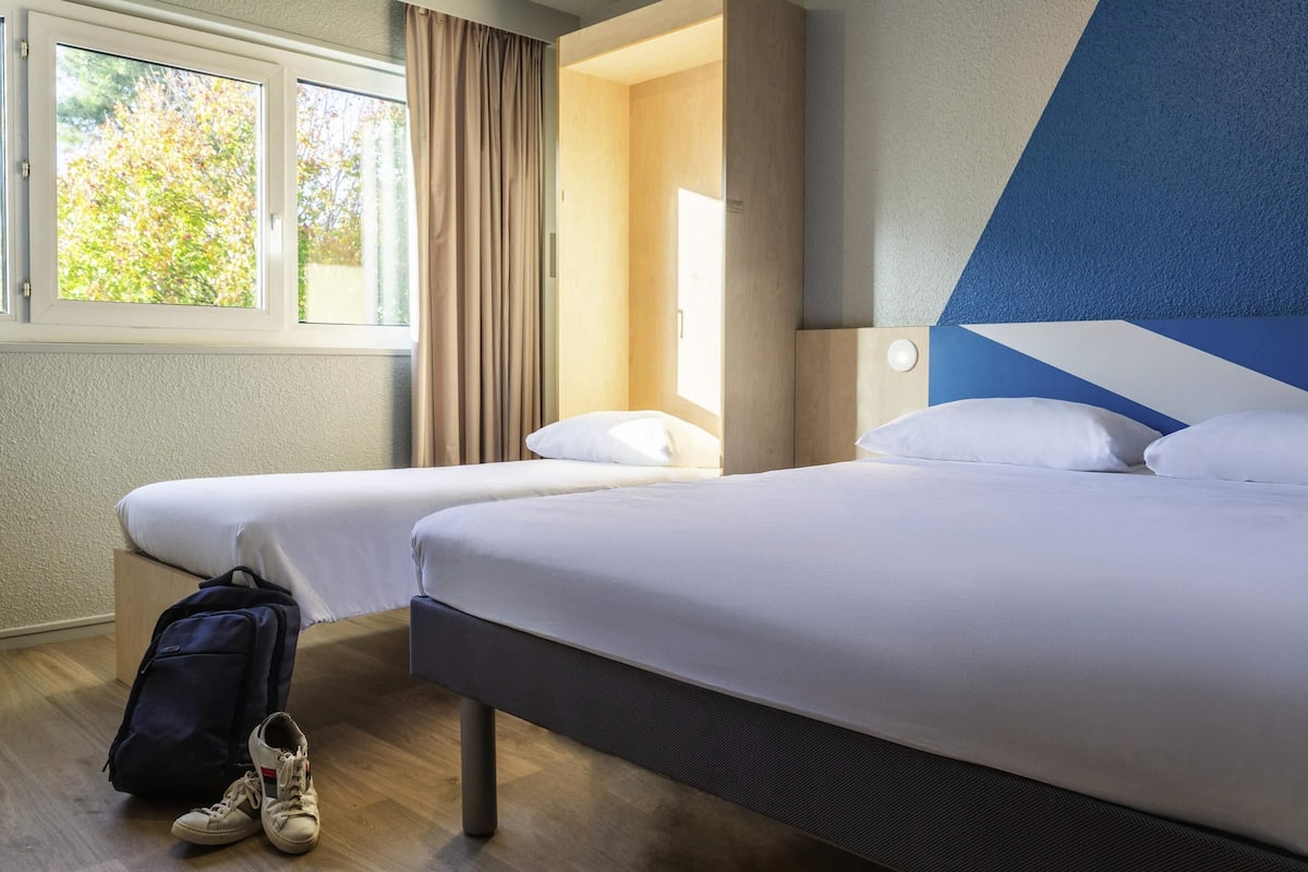 Een hotelkamer met twee bedden, een raam met gordijnen, een houten vloer en een wanddecoratie in blauw en wit.