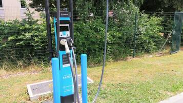 Een blauw laadstation voor elektrische voertuigen met een QR-code, buiten gelegen met een gazon en een hek op de achtergrond.