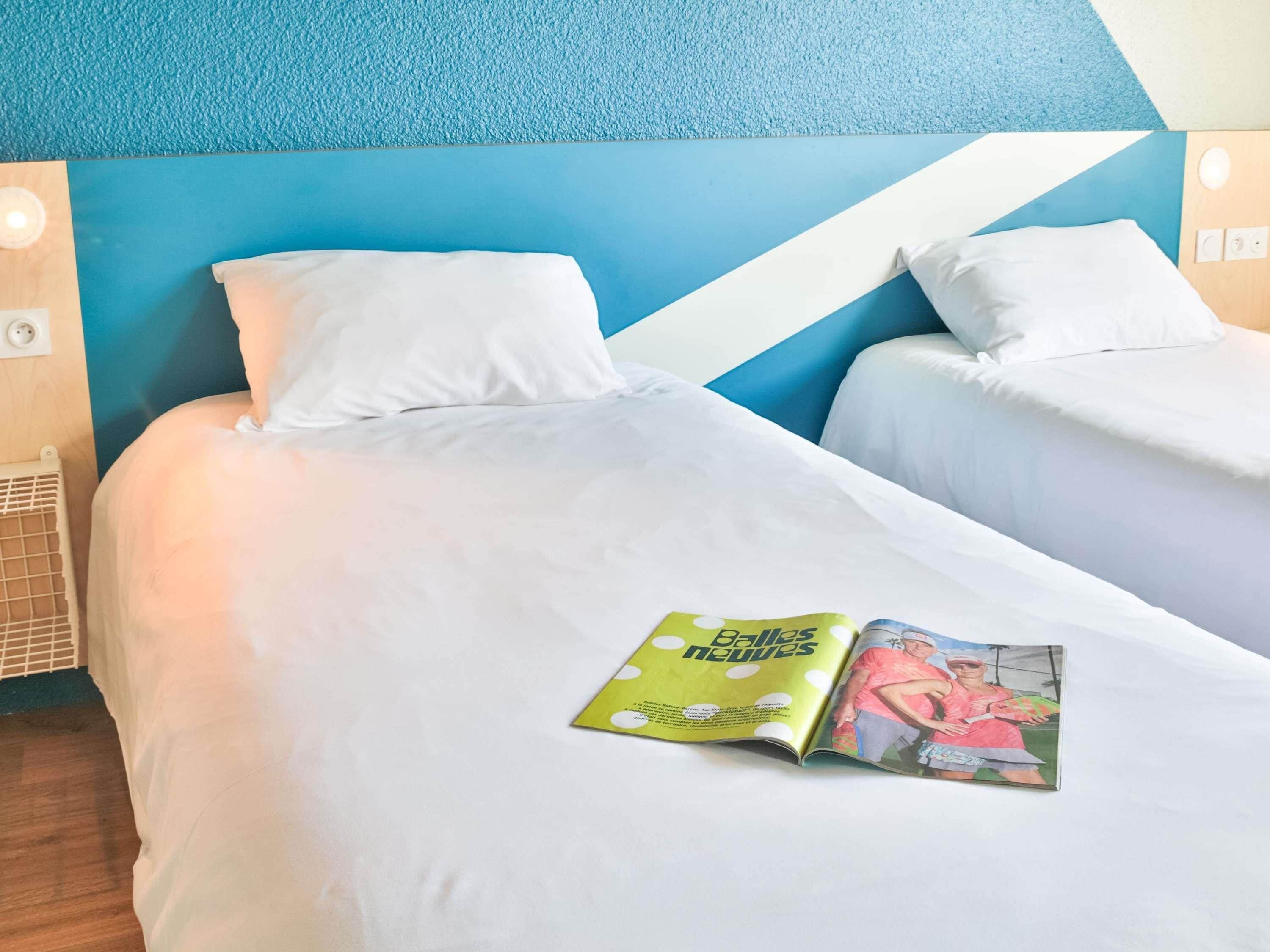 A hotel room with two beds, a magazine on the bed, and a blue and white wall design.
