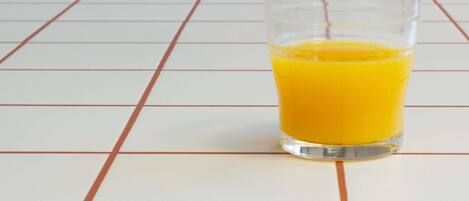 Un vaso de jugo de naranja sobre un piso de baldosas.