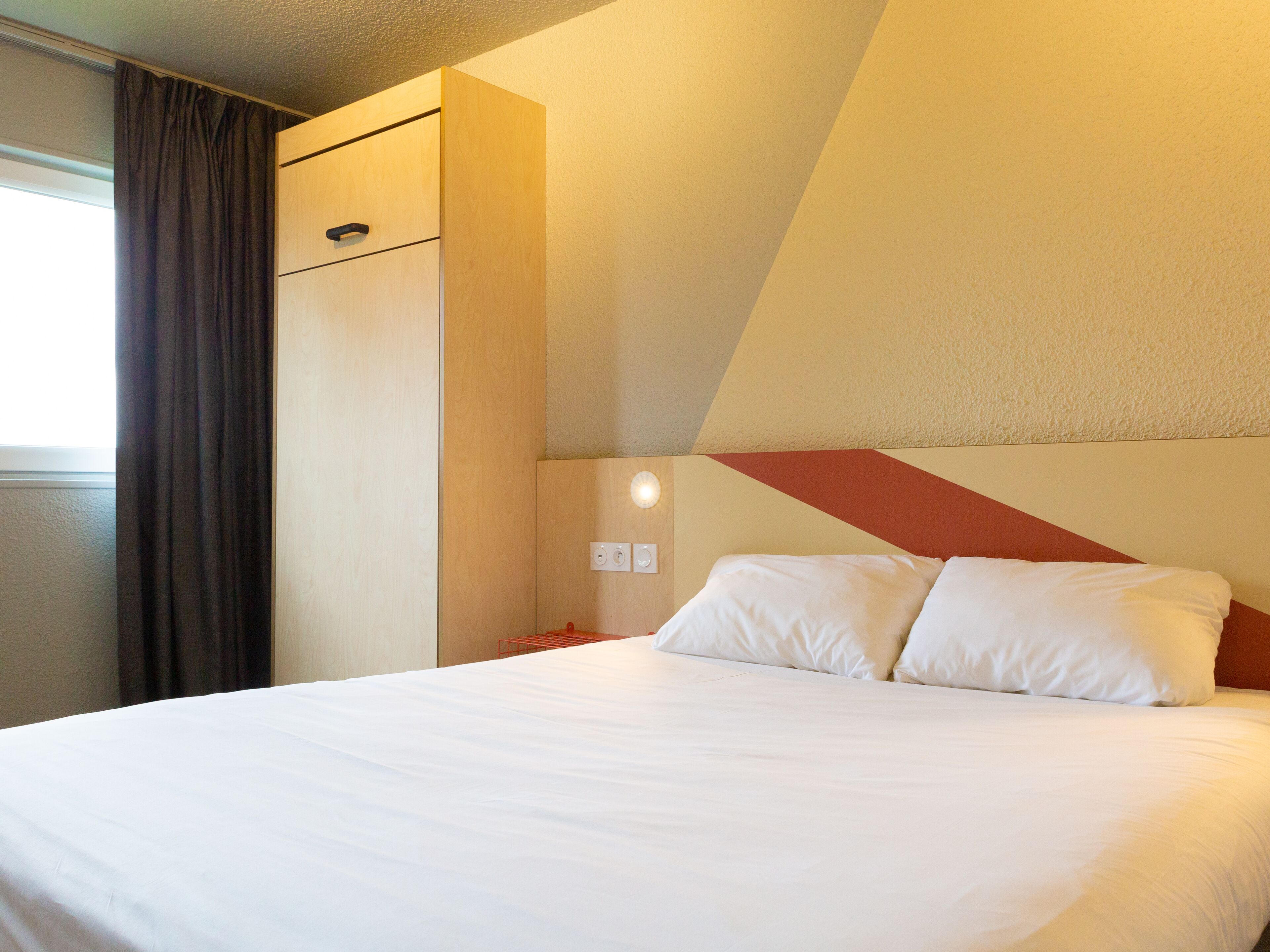 A hotel room with a bed, a wardrobe, and a wall-mounted light fixture.