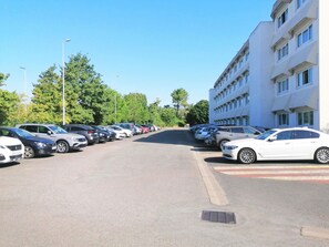 Un parcheggio con diverse auto, un edificio con molte finestre e alberi sullo sfondo.