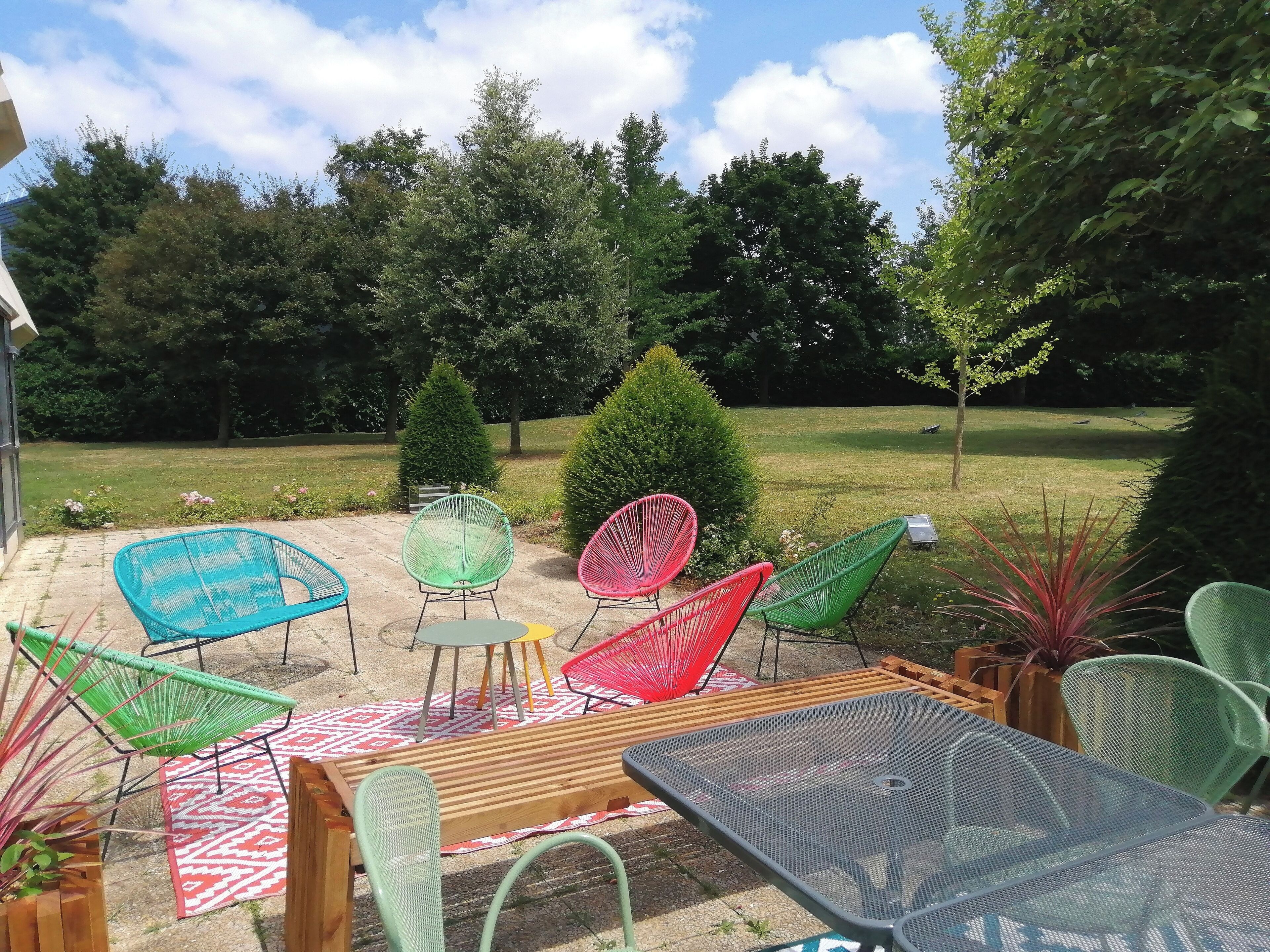 An outdoor patio with a table and chairs, a patterned rug, and a view of a grassy area with trees.