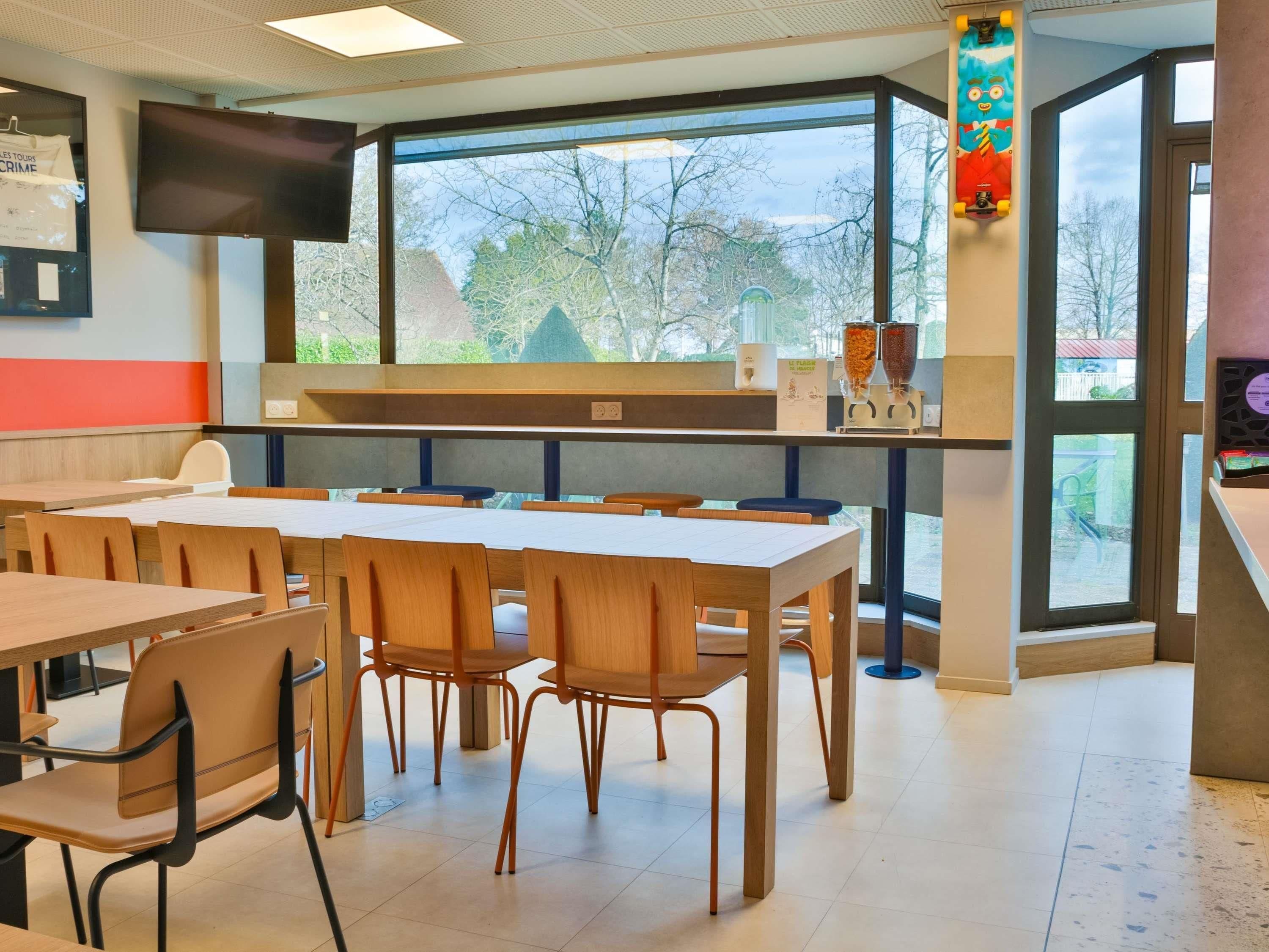 Une salle de classe avec des tables et des chaises, une grande fenêtre et un téléviseur fixé au mur.