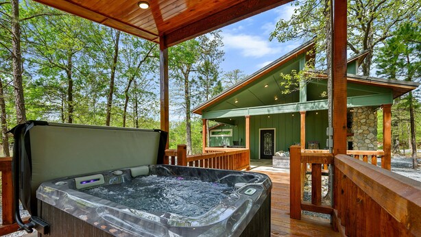 A hot tub on a wooden deck with a view of a cabin and surrounding trees. - Butterfly Kisses- Perfect Honeymoon Cabin! (Broken Bow)