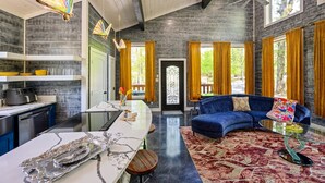 A modern kitchen with a marble countertop, a dining area with a blue sofa and a glass coffee table, and a view of the outdoors through large windows. - Butterfly Kisses- Perfect Honeymoon Cabin! (Broken Bow)