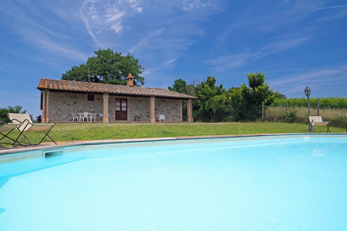 A stone building with a tiled roof, a swimming pool, and outdoor seating.