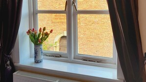 Et vindue med to rammer, gardiner og en vase med blomster på et vindueskar.