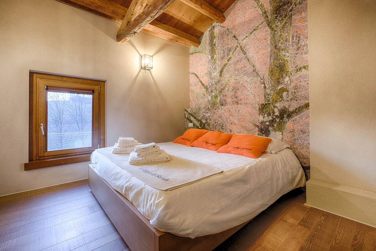 Ein Schlafzimmer mit einem Bett, einem Fenster, einer Wandleuchte und einer Holzbalkendecke.