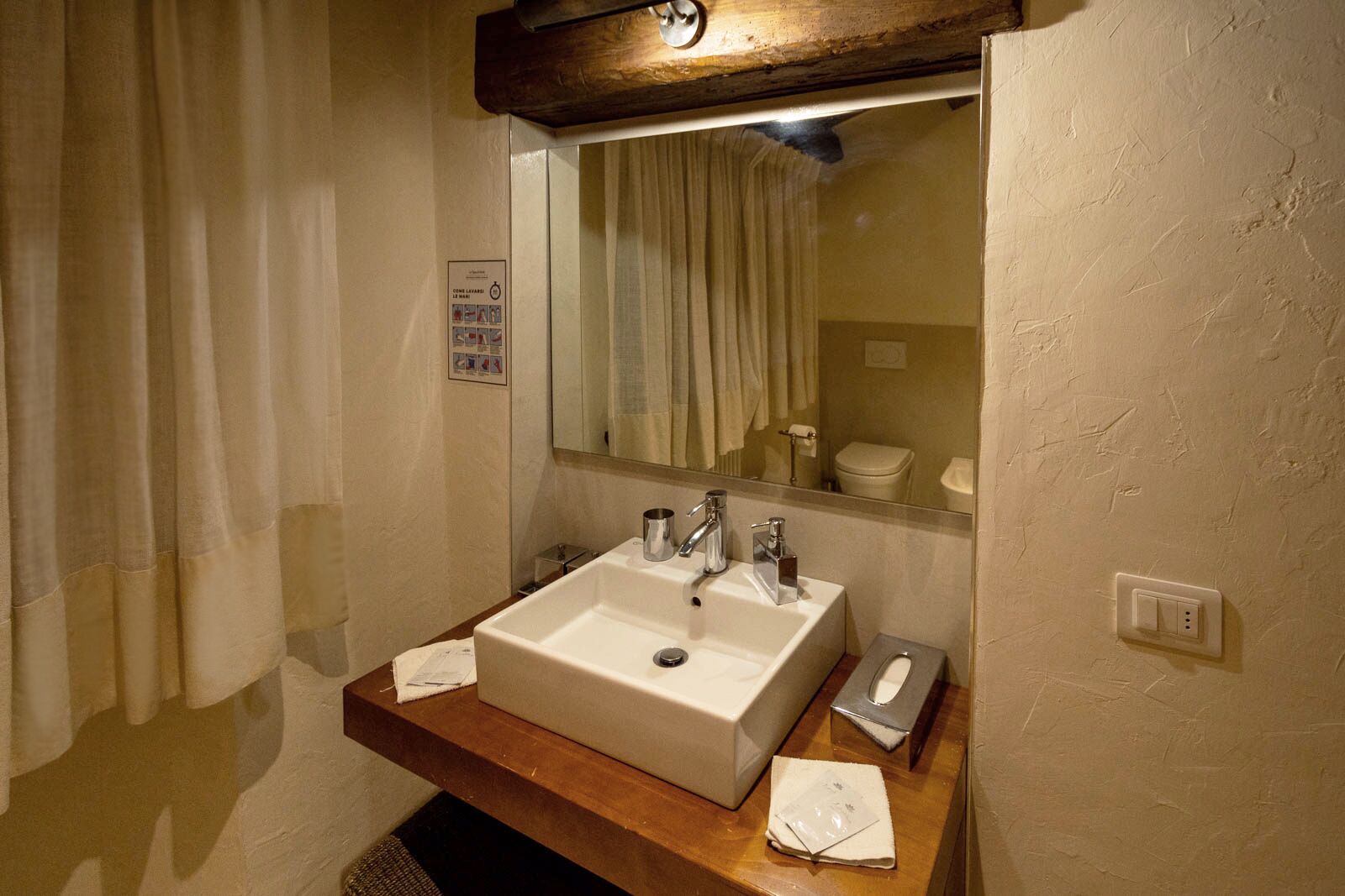 A bathroom with a white sink, two faucets, a mirror, and a wooden shelf.