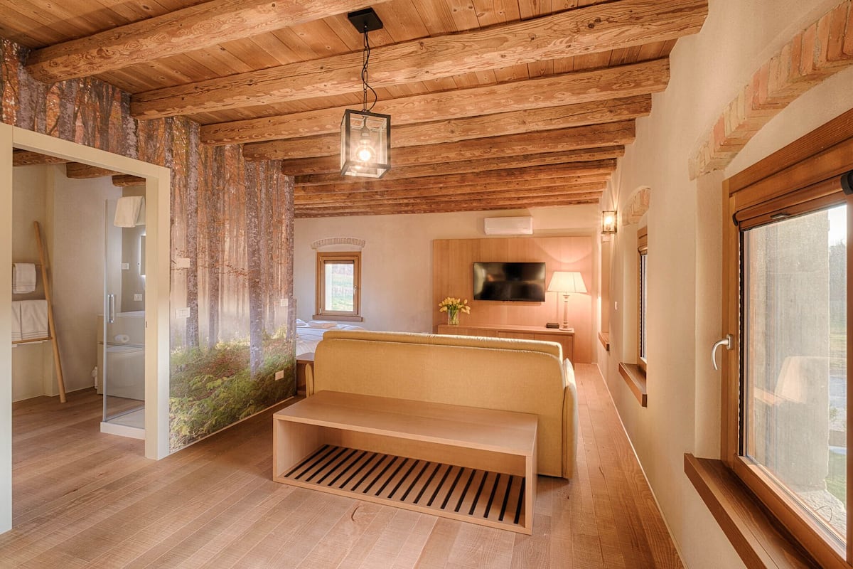 Ein gemütliches Zimmer mit Holzbalkendecke, einer Bank, einem Fernseher und einem Fenster.