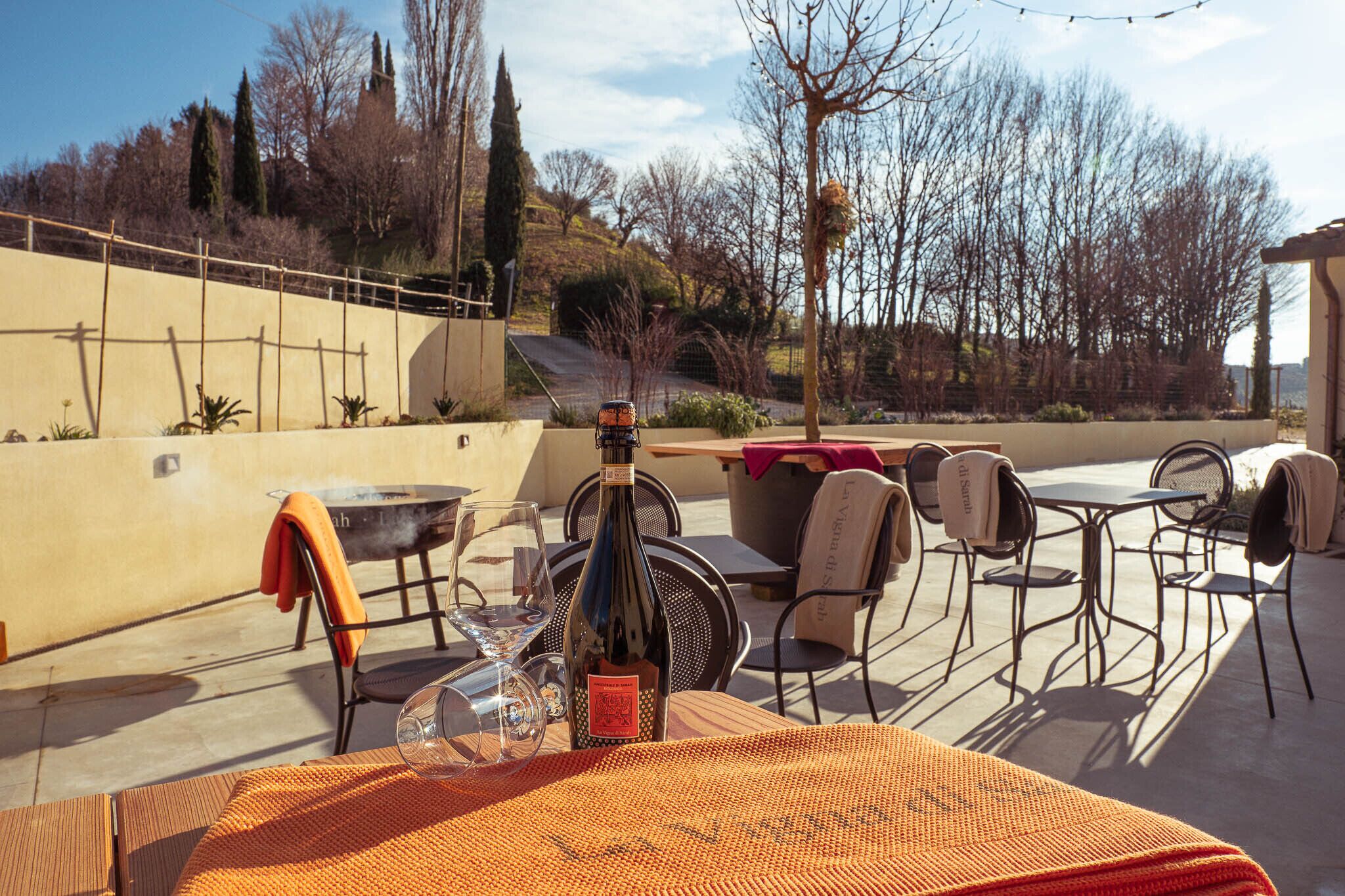 An outdoor patio with a table, chairs, a bottle of wine, and a glass.
