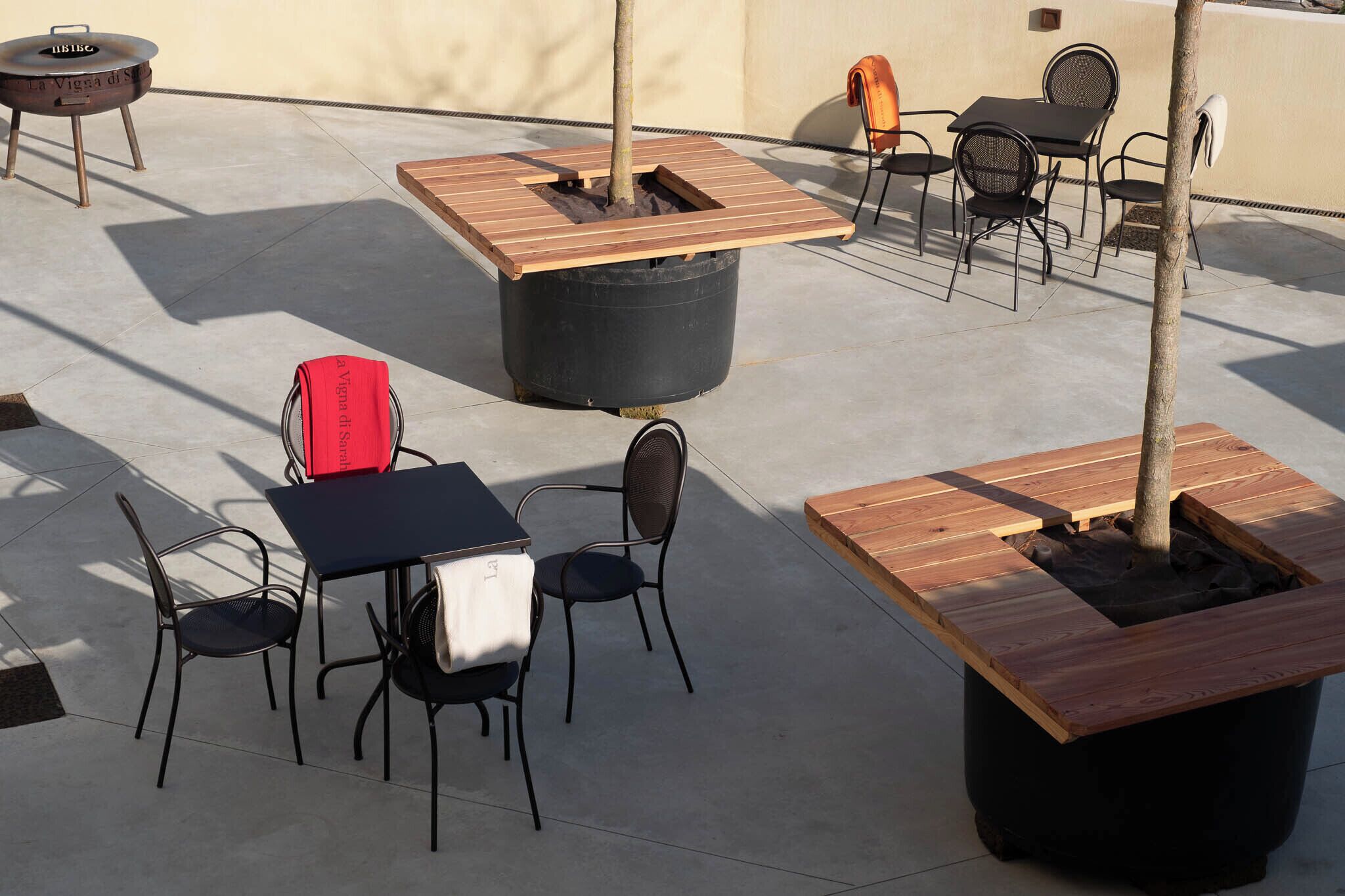 Un'area esterna con tavoli, sedie, un barbecue e fioriere con alberi.