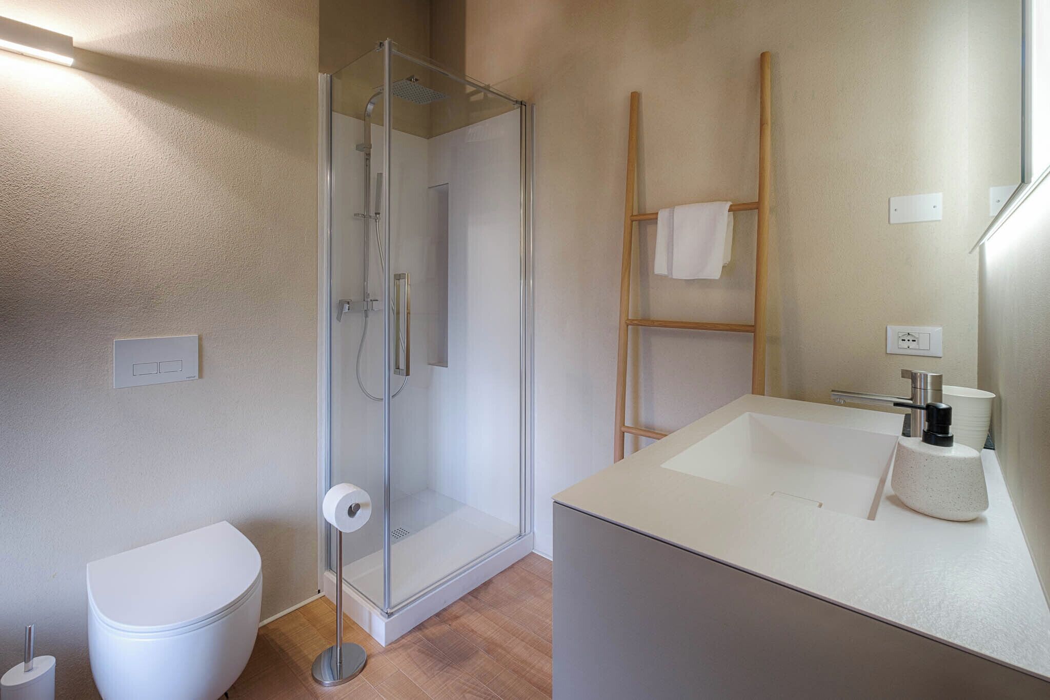 Ein modernes Badezimmer mit einer gläsernen Duschkabine, einer weißen Toilette und einem großen Waschbecken mit Spiegel.