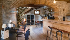 Een rustiek interieur met stenen muren, houten balken en een bar met krukken en wijnglazen.