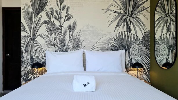 Une chambre d’hôtel avec un grand lit, du linge de lit blanc et une fresque murale représentant des plantes tropicales.
