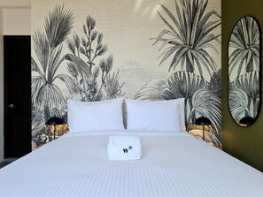 Ein Hotelzimmer mit einem großen Bett, weißer Bettwäsche und einer Wandmalerei von tropischen Pflanzen.
