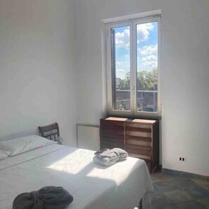Een slaapkamer met een bed, een houten dressoir en een raam met uitzicht op bomen en een hek.