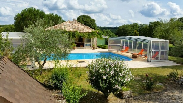 A swimming pool with a glass enclosure, a small house, and surrounding greenery.